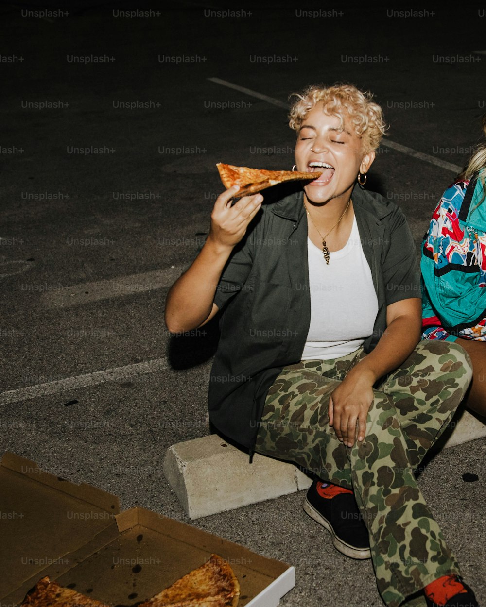 Eine Frau, die auf dem Boden sitzt und ein Stück Pizza isst