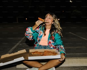 a woman sitting on the ground eating a slice of pizza