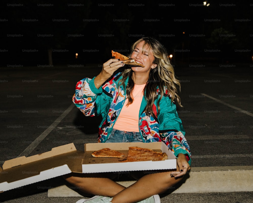 una donna seduta a terra che mangia una fetta di pizza