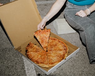 a woman sitting on the ground with a pizza in a box