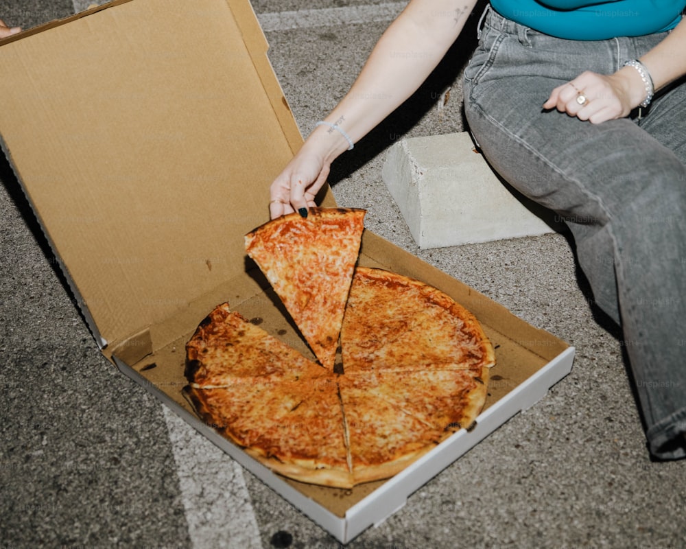 Eine Frau, die mit einer Pizza in einer Schachtel auf dem Boden sitzt