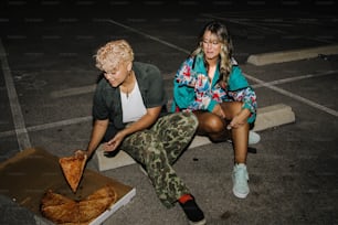 a man and a woman sitting on the ground eating pizza