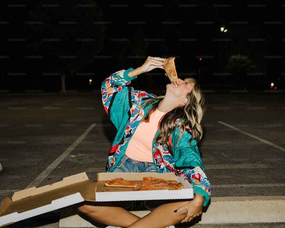 Eine Frau, die auf dem Boden sitzt und ein Stück Pizza isst