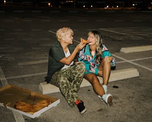 two people sitting on the ground eating pizza