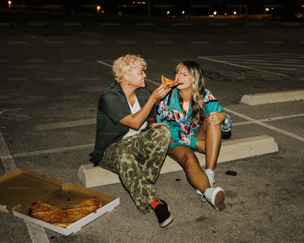 two people sitting on the ground eating pizza