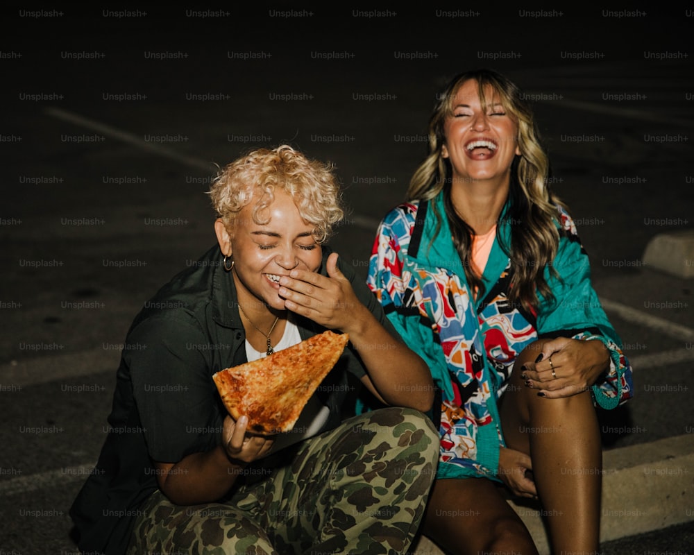 Un couple de femmes assises l’une à côté de l’autre mangeant une part de pizza