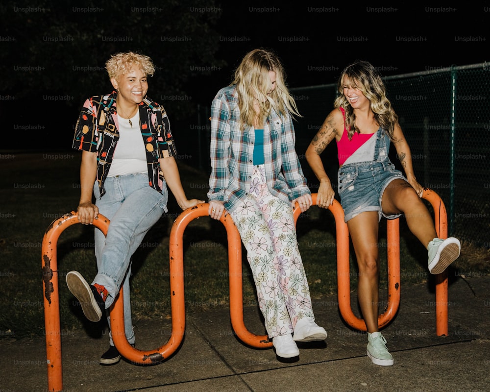 a group of three women sitting on top of a metal fence