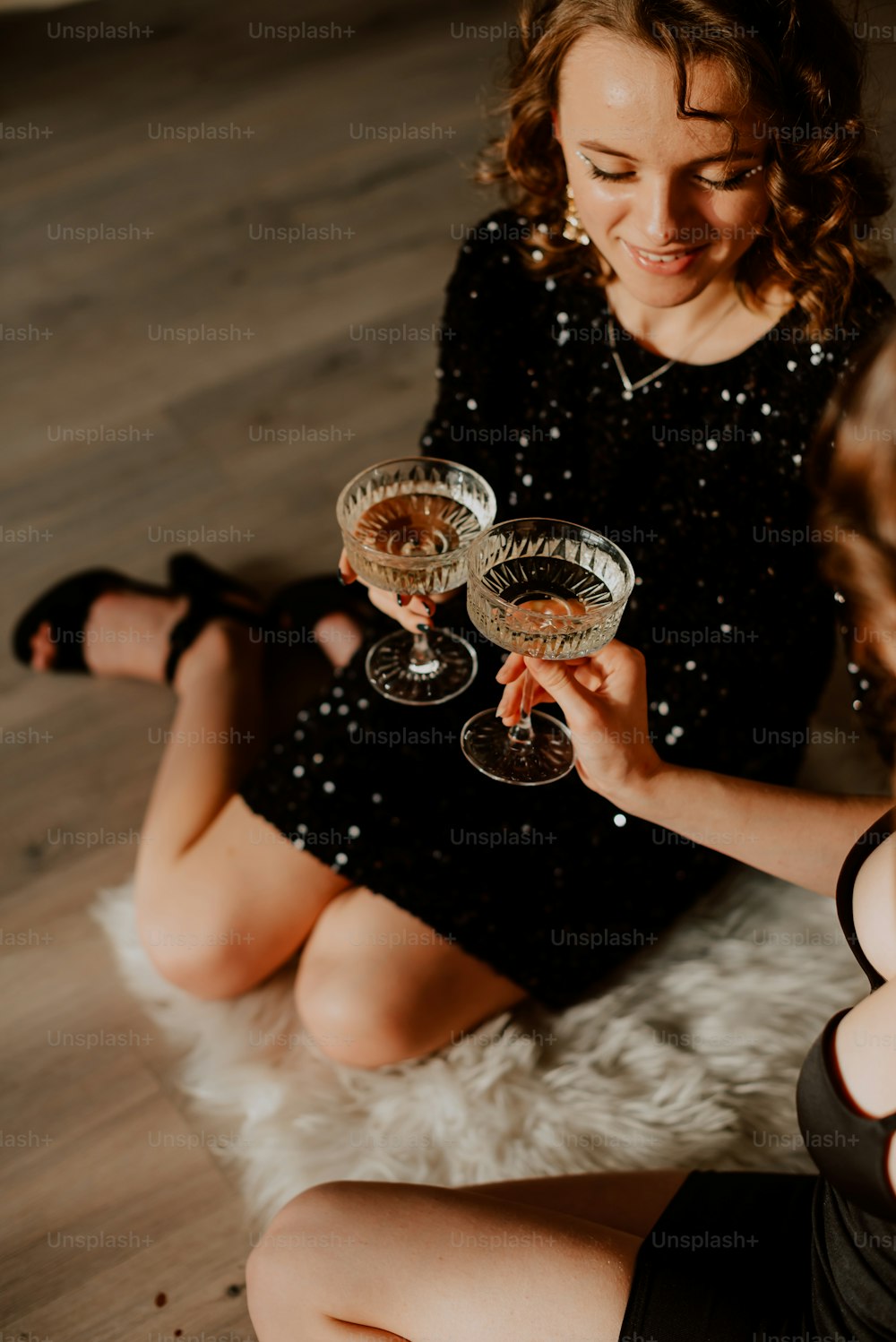 두 개의 와인잔을 들고 바닥에 앉아 있는 여자