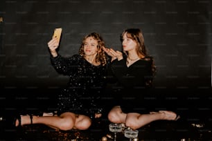 two women sitting next to each other holding up a cell phone