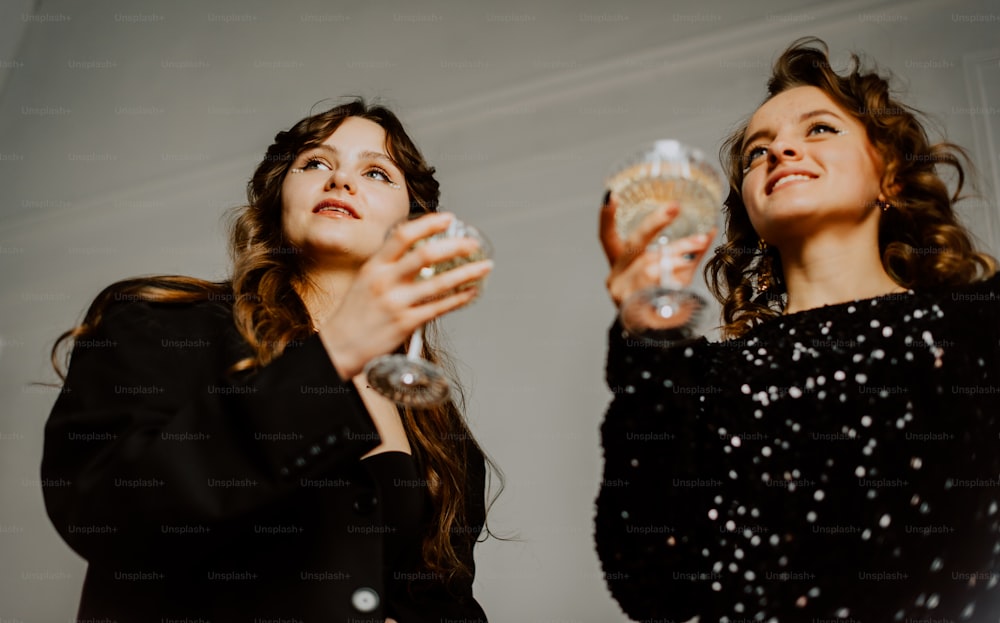 Un couple de femmes debout l’une à côté de l’autre tenant des verres de vin