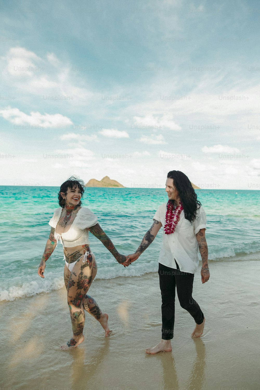 two women holding hands while walking on the beach