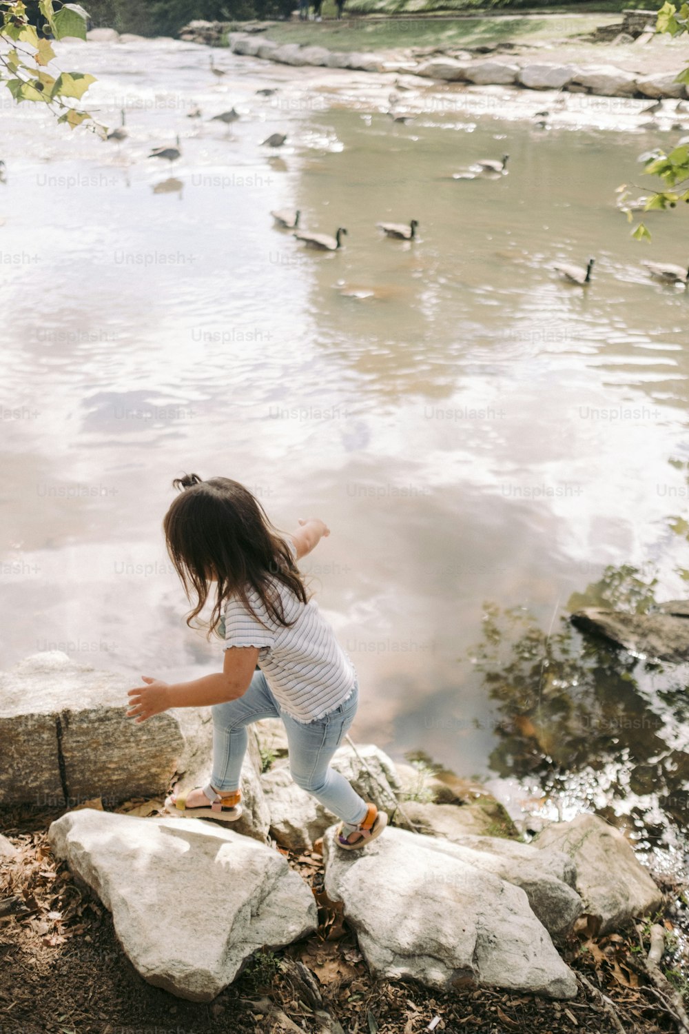 a little girl standing on a rock next to a body of water