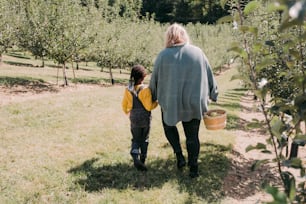 a woman and child walking through an apple orchard