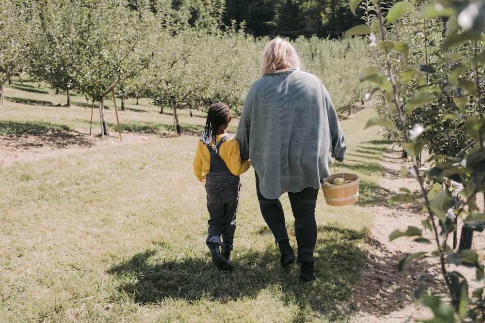 uma mulher e uma criança caminhando por um pomar de maçãs
