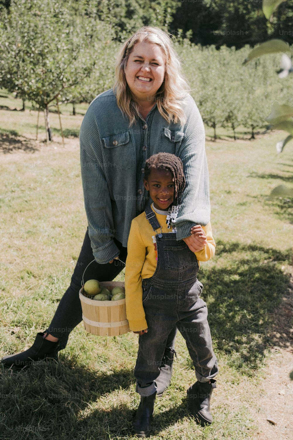 a woman holding a basket of apples while standing next to a child