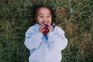 a little girl laying in the grass with an apple