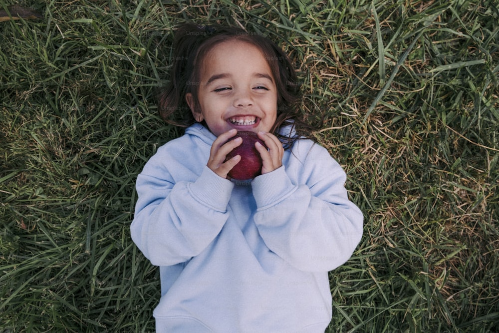 a little girl laying in the grass with an apple
