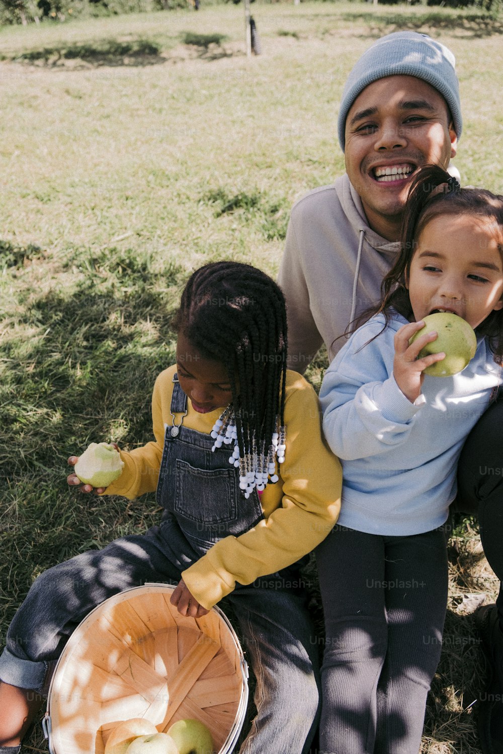 a man and two children sitting on the ground eating apples