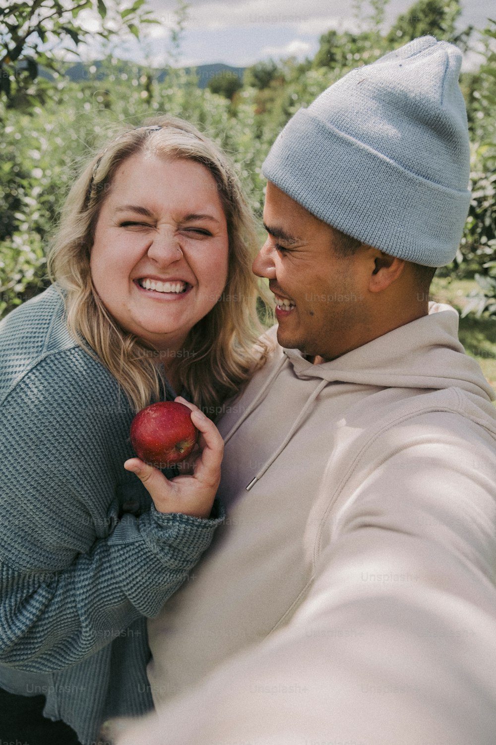 a man and a woman smile as they hold an apple
