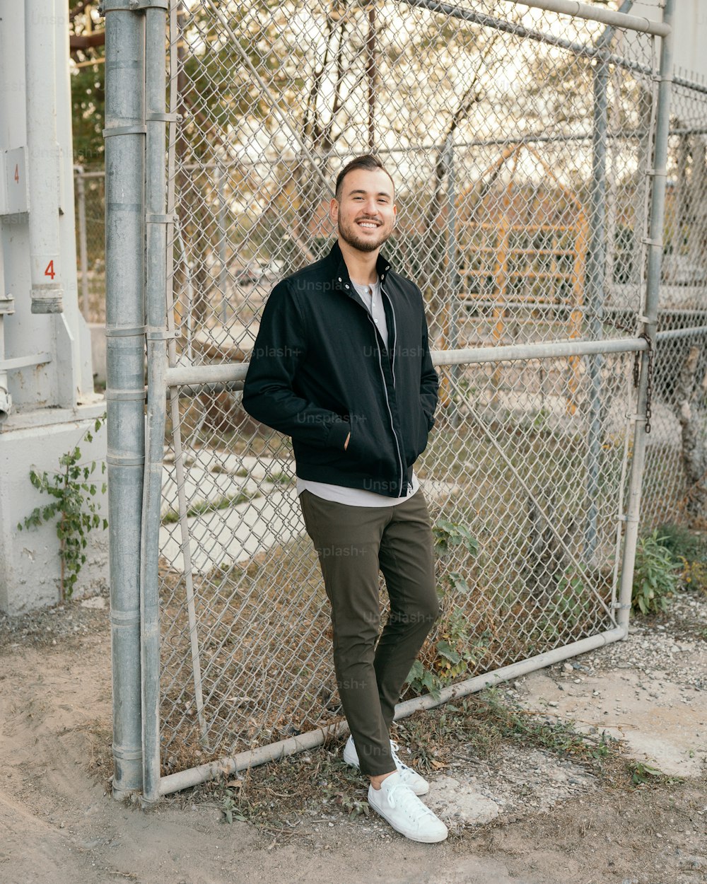 a man standing in front of a fence with his hands in his pockets