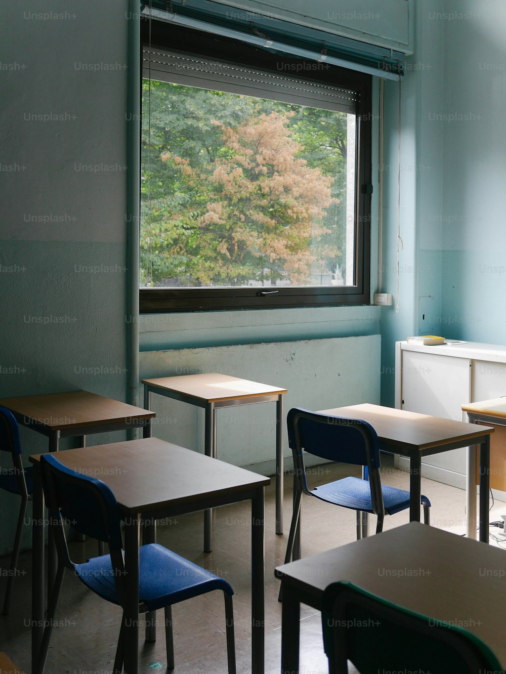 uma sala de aula com carteiras, cadeiras e uma janela