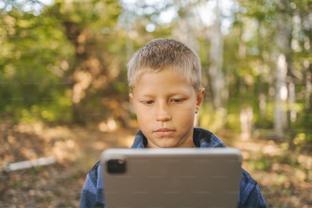 a young boy looking at a laptop in the woods