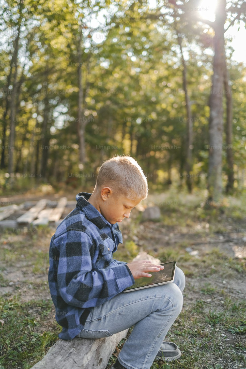 a young boy sitting on a log using a laptop