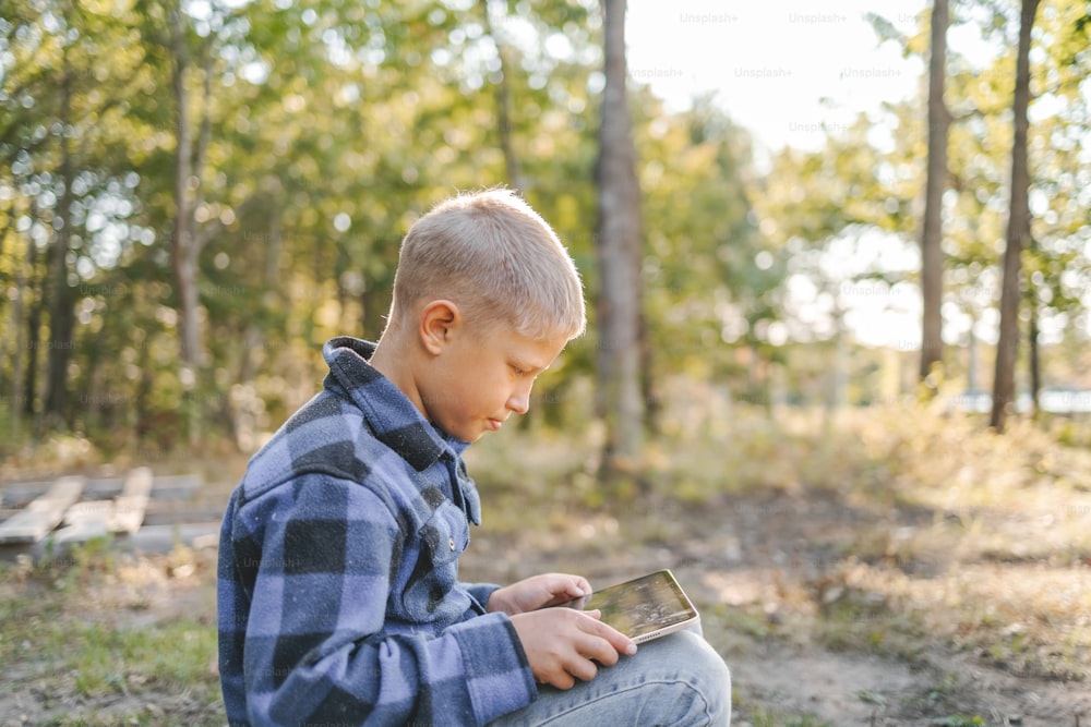 a young boy sitting in the woods looking at a cell phone