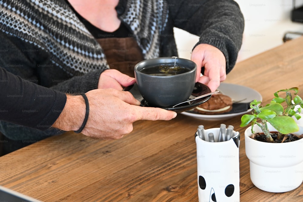 uma mulher segurando uma xícara de café enquanto está sentada em uma mesa