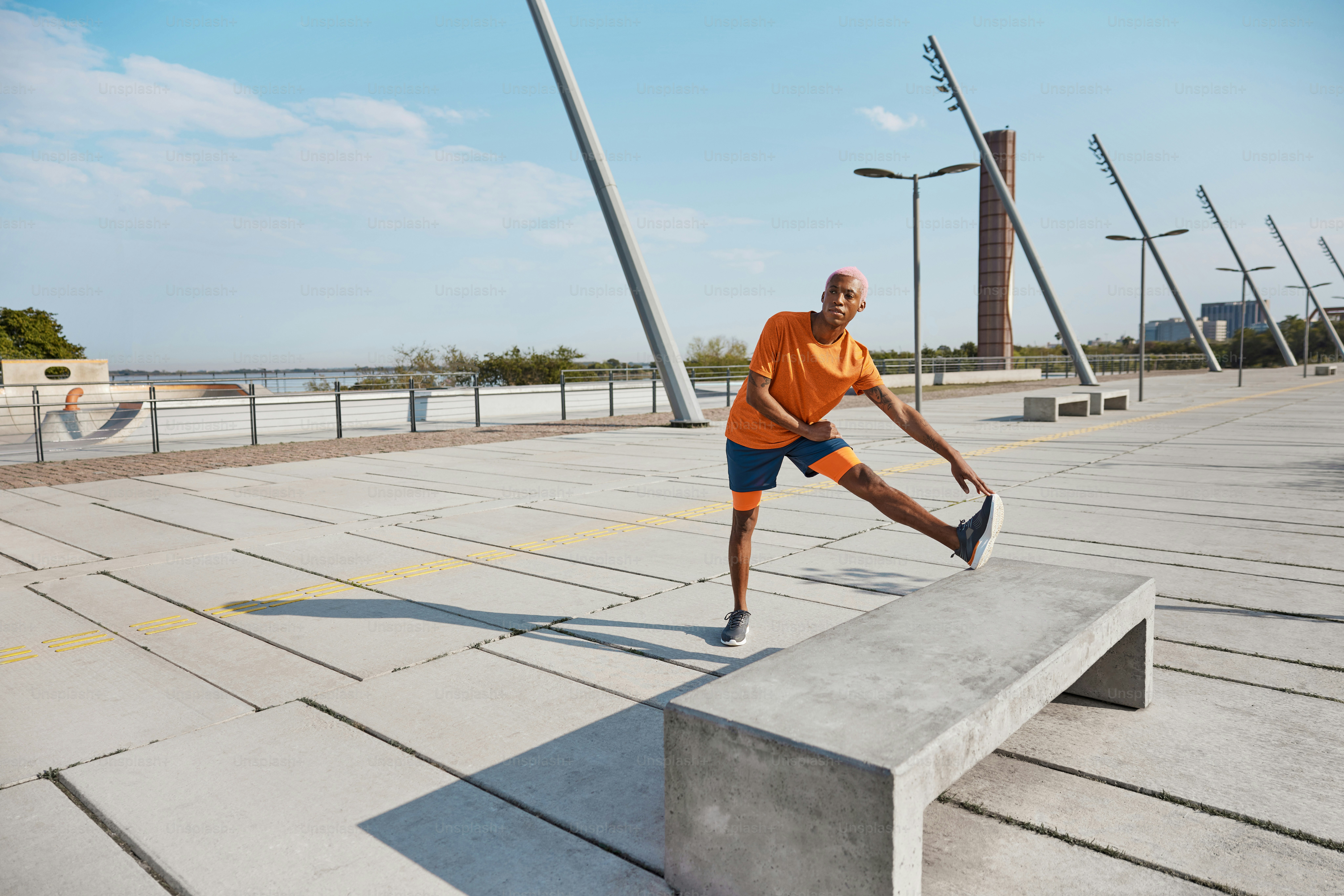 Um homem de camisa laranja está fazendo um truque em um banco de concreto
