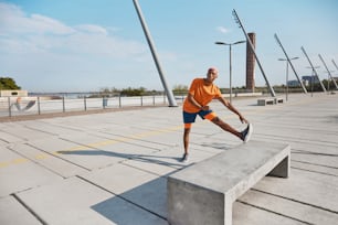 Um homem de camisa laranja está fazendo um truque em um banco de concreto