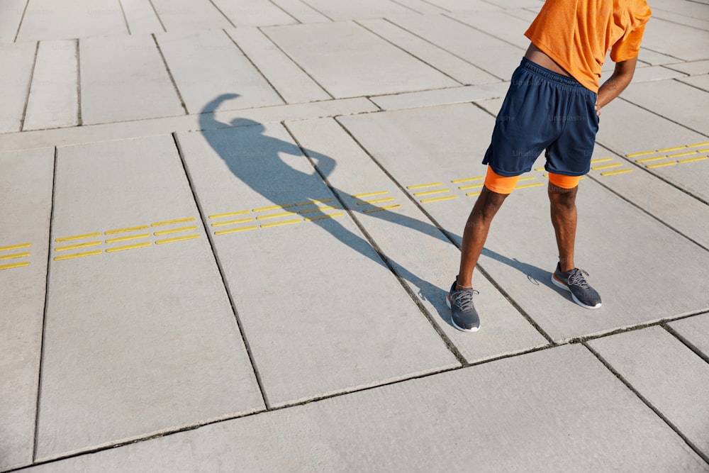 um homem parado em uma calçada com sua sombra no chão