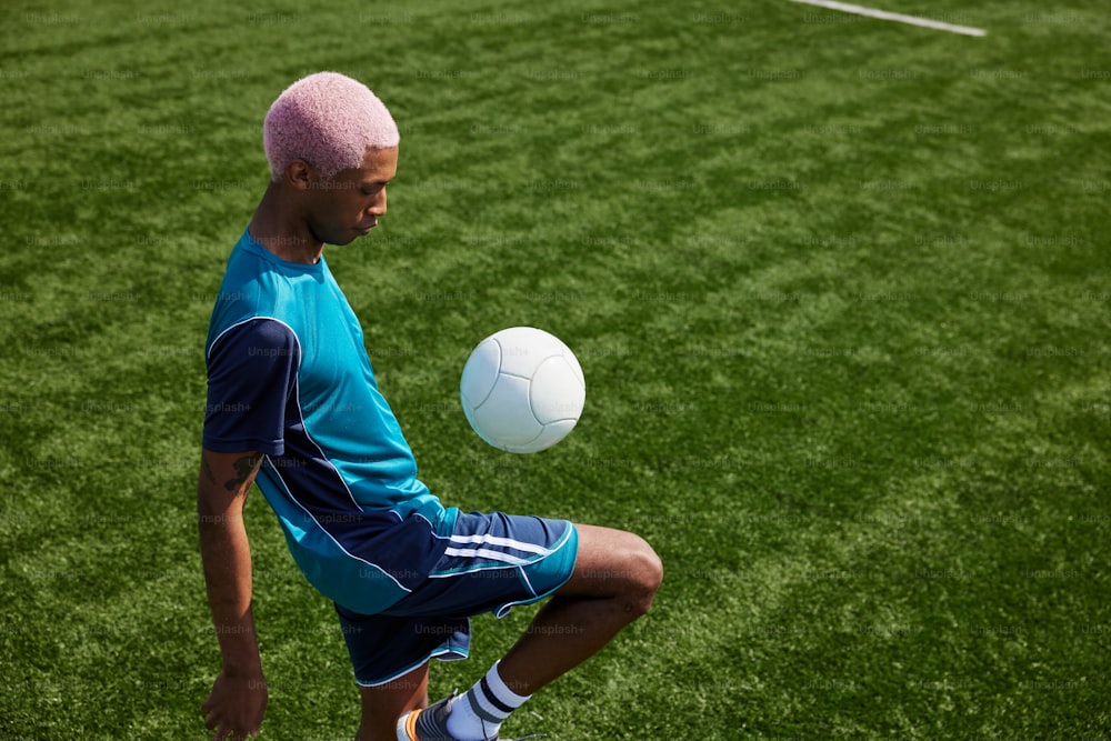 Um homem com um cabelo rosa está brincando com uma bola de futebol