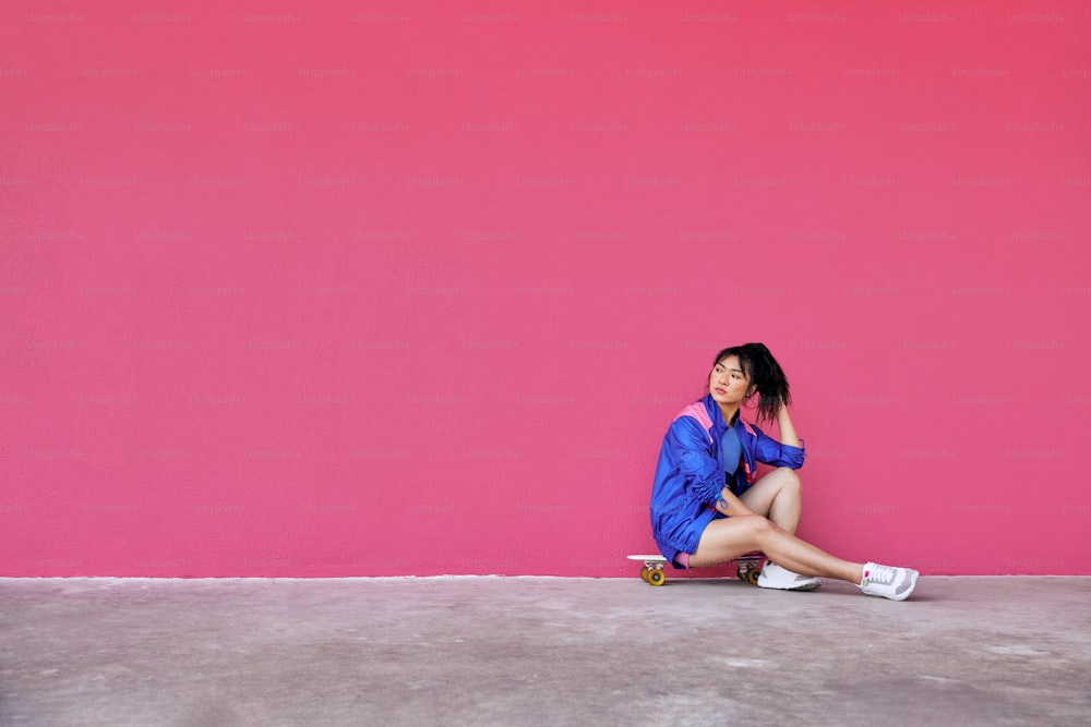 a woman sitting on the ground in front of a pink wall