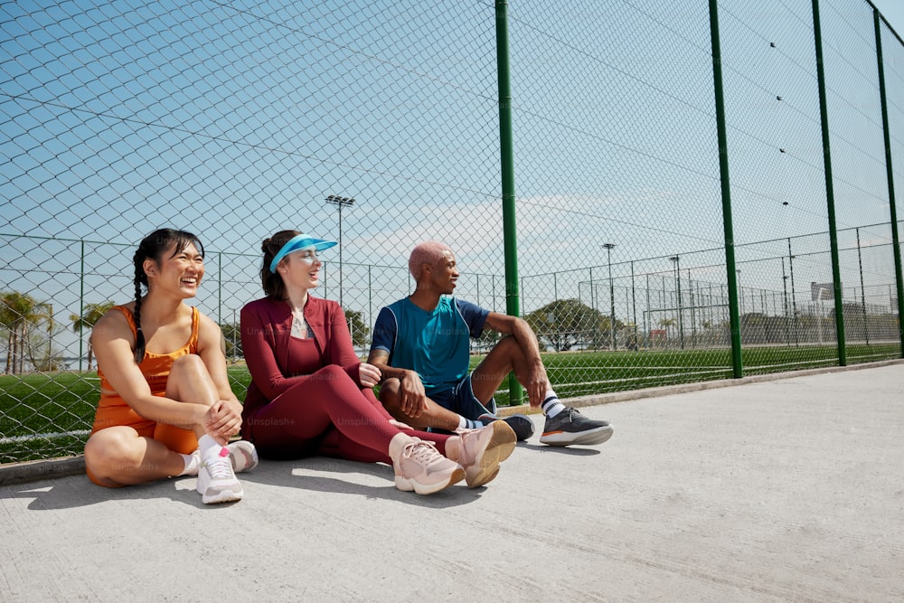 a group of people sitting on the ground near a fence