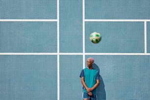 Un hombre parado frente a una pared azul con una pelota de fútbol en el aire