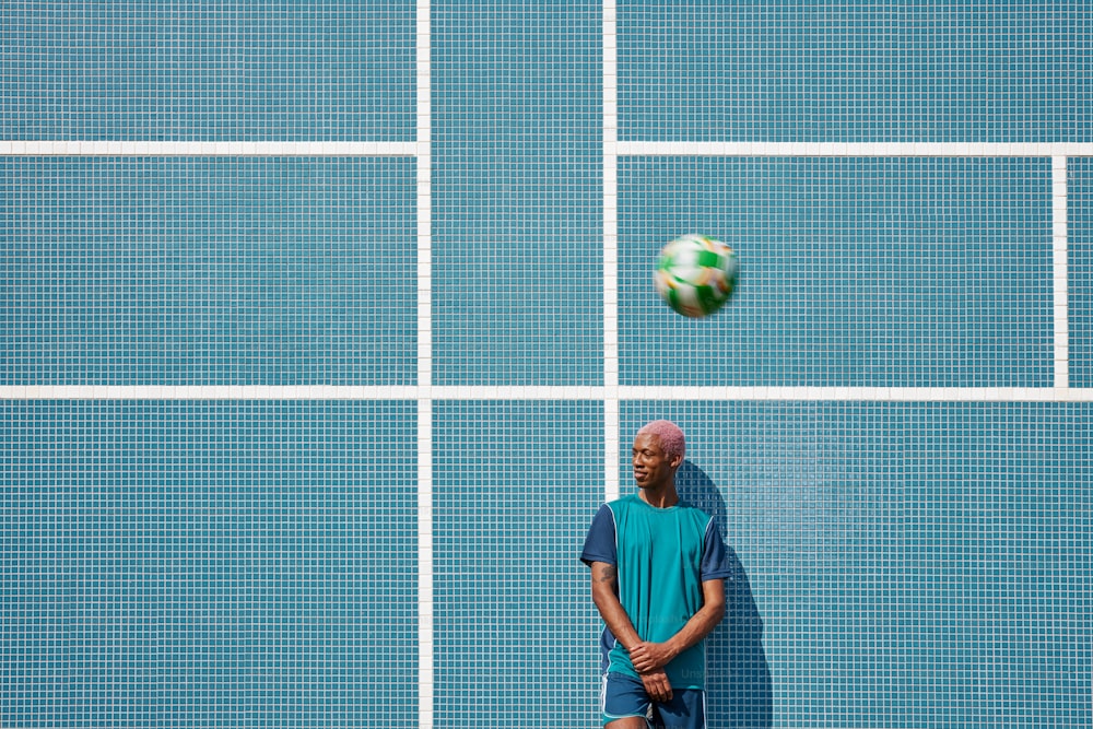 Un uomo in piedi di fronte a un muro blu con un pallone da calcio in aria
