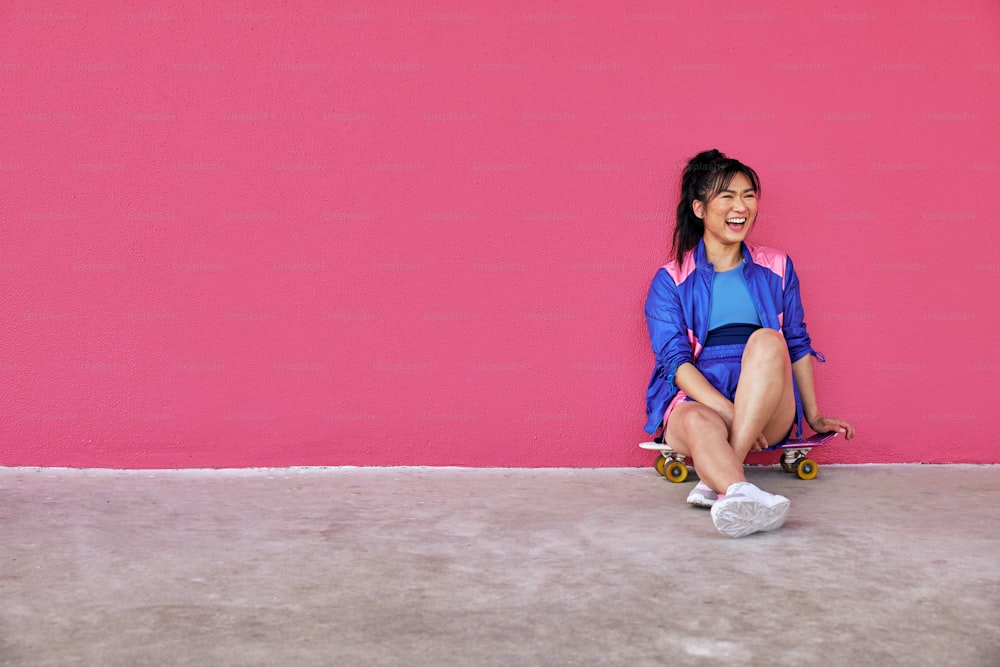 Une femme assise sur une planche à roulettes devant un mur rose