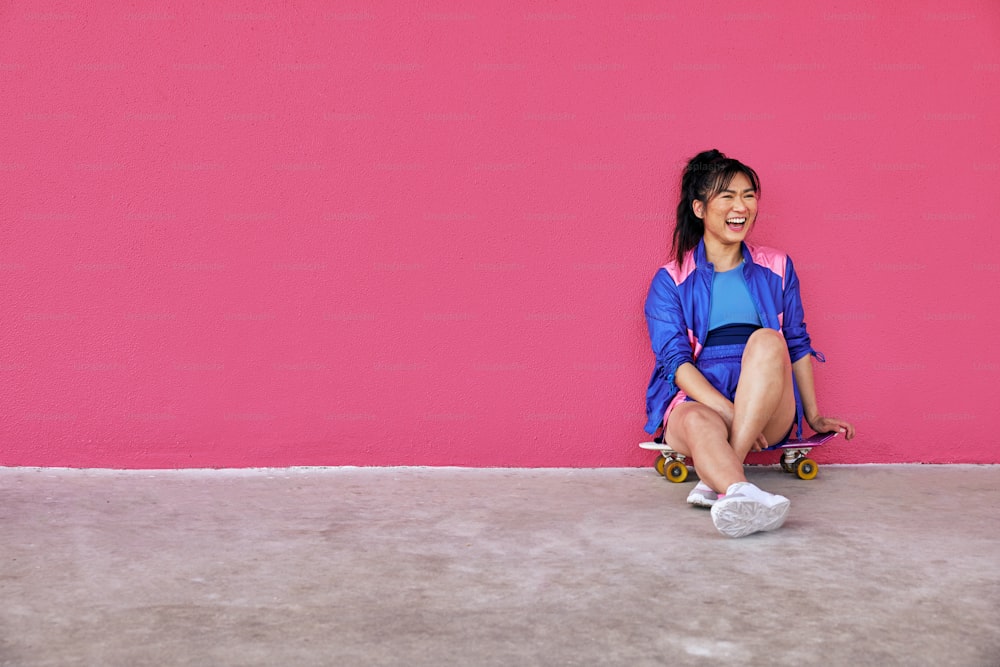 a woman sitting on a skateboard in front of a pink wall