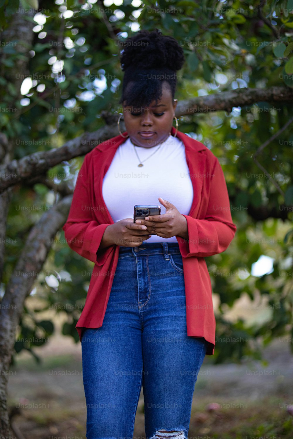 Una mujer parada debajo de un árbol mirando su teléfono celular
