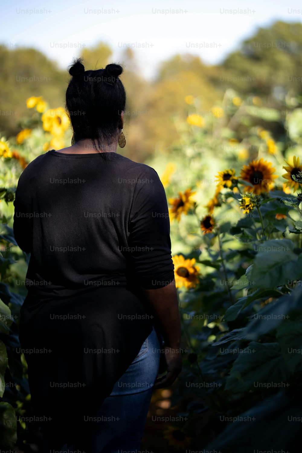 a woman walking through a field of sunflowers