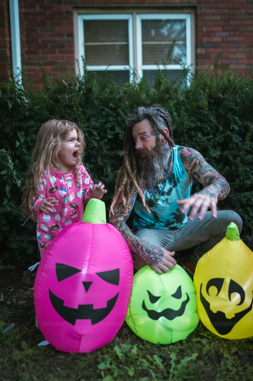 a man sitting next to a little girl next to three inflatable pumpkins