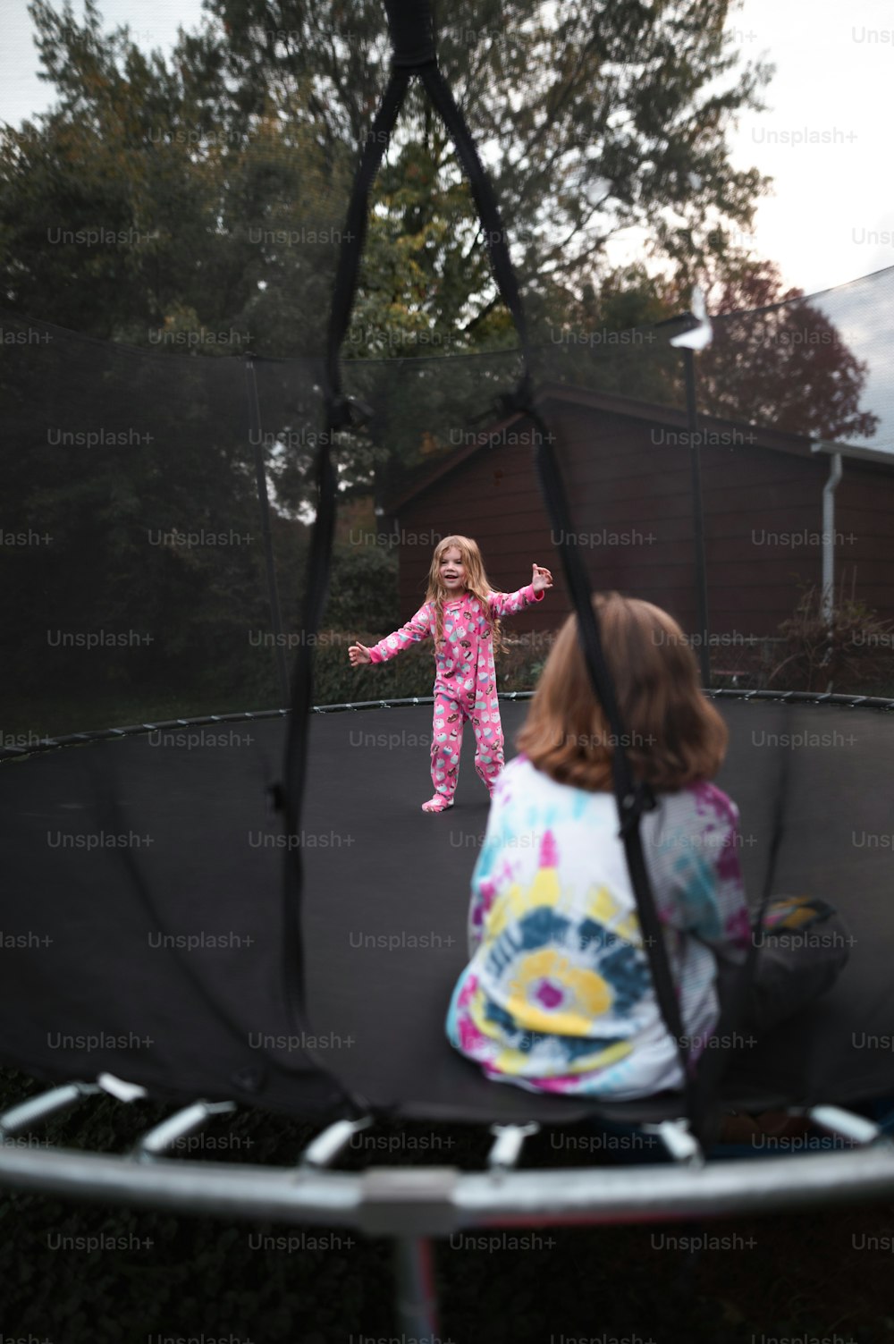 two young girls playing on a trampoline in a backyard
