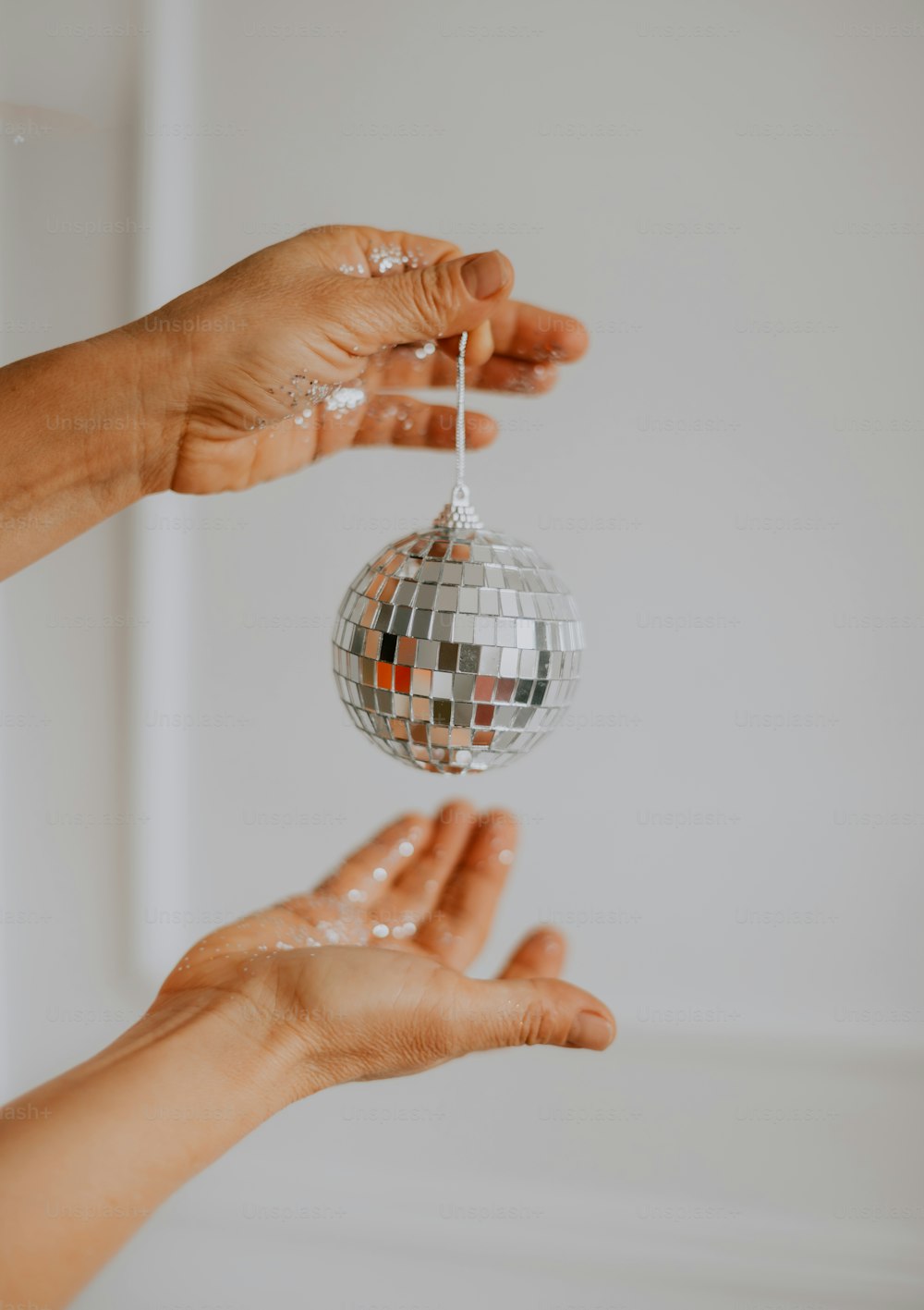 two hands are holding a disco ball ornament
