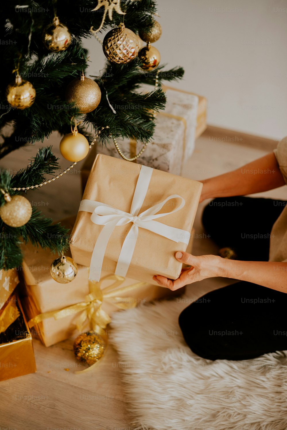 a woman sitting on the floor holding a wrapped present under a christmas tree