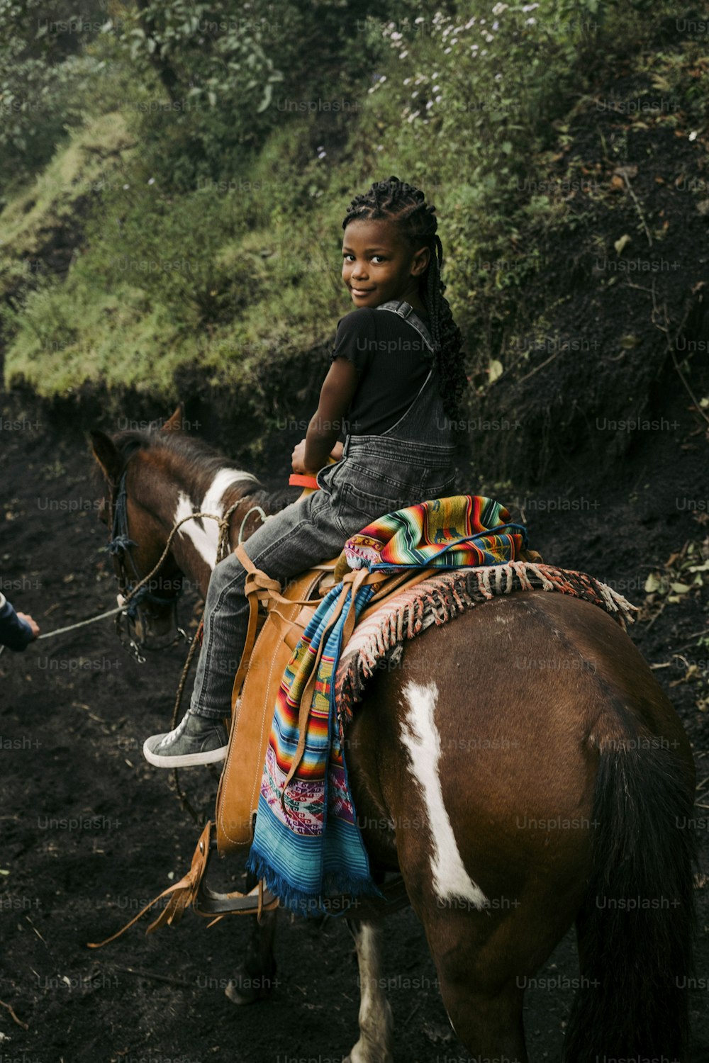 Ein kleines Mädchen, das auf dem Rücken eines braun-weißen Pferdes reitet