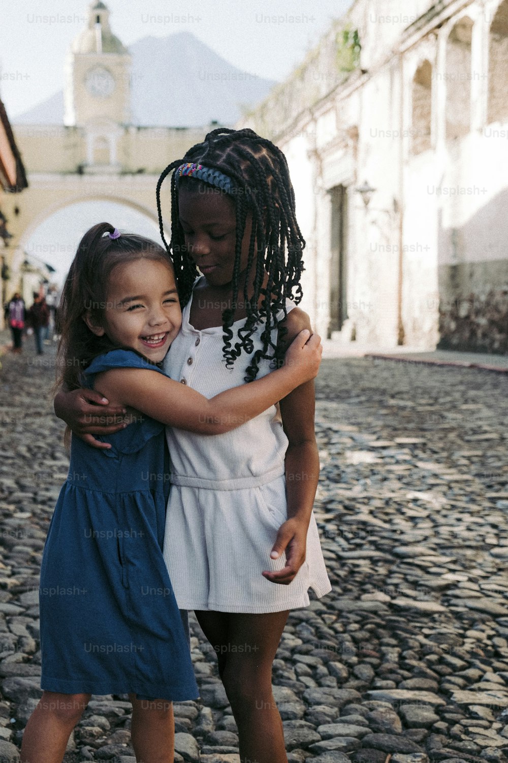 two young girls hugging each other on a cobblestone street