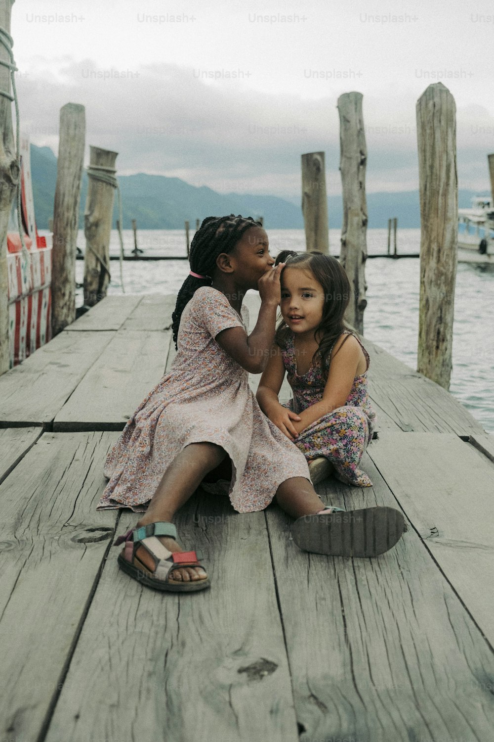 two young girls sitting on a dock next to each other