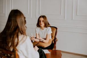 a woman sitting in a chair talking to another woman