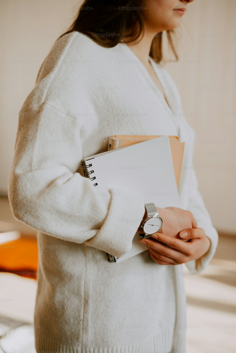 Una mujer con un suéter blanco sosteniendo un cuaderno y un reloj